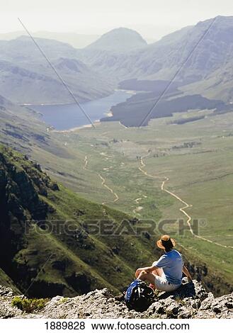 Stock Photo - Hiker Looking At View, Sitting On Top Of Mountain, Rear View. Fotosearch