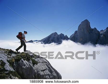 Stock Photo - Hiker On Mountain Peak Surrounded By Clouds. Fotosearch