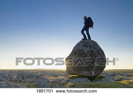 Stock Image - Hiker Standing On Head-Shaped Boulder. Fotosearch