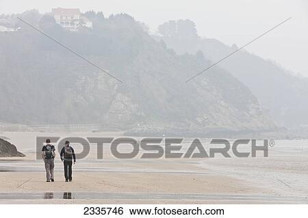 Stock Photograph - Hikers Walking Along Sands On North Beach; Pembrokeshire Coast, Wales, United Kingdom. Fotosearch