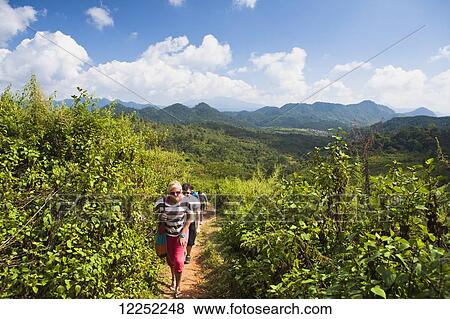 Hiking on a trail through lush foliage with a mountainous landscape in the distance; Hintang, Laos View Large Photo Image Stock Photo - Hiking on a trail through lush foliage with a mountainous landscape in the distance; Hintang, Laos. Fotosearch