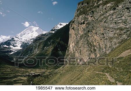 Stock Photo - Himalayas; Bhutan, Remote farmland surrounded by cliffs and snow-covered mountains. Fotosearch