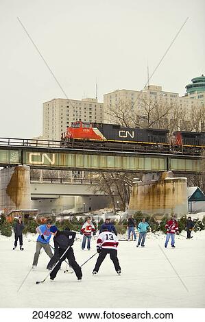 Stock Image - Hockey Game On A Pond As A Cn Train Passes Overhead, Forks Historic Port, Assiniboine River, Winnipeg, Manitoba. Fotosearch