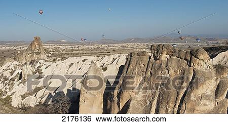 Stock Photograph - Hot Air Balloons Fill The Blue Sky Over A Rugged Landscape; Nevsehir Turkey. Fotosearch