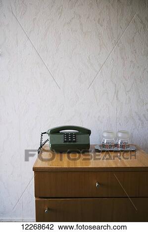 Stock Image - Hotel nightstand with push-button phone and water glasses, textured wallpaper; Kiev, Ukraine. Fotosearch