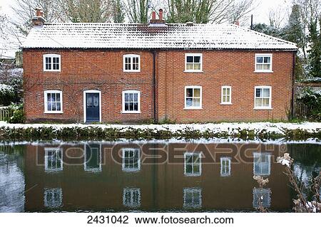Stock Image - House on the edge of a canal reflected in the tranquil water; Winchester, Hampshire, England. Fotosearch