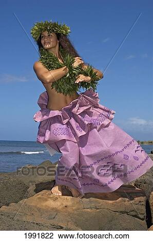 Stock Image - Hula Dancer With Haku Lei In Traditional Outfit On Rocky Coast, Ocean Background. Fotosearch