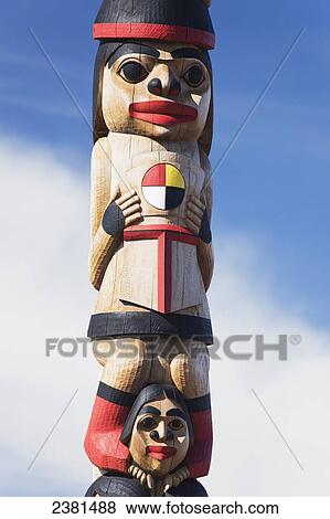 Stock Photo - Human figures carved and painted on a wooden totem pole against a blue sky; Whitehorse, Yukon, Canada. Fotosearch