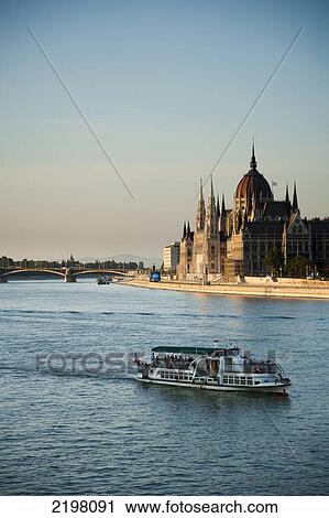 Stock Image - Hungary, past Hungarian Parliament Building; Budapest, Tourist boats passing along Danube river. Fotosearch