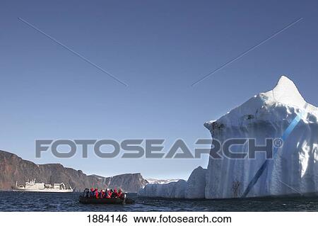 Stock Photograph - Iceberg And Tourists On An Inflatable Raft With Their Boat In The Background; Devon Island, Nunavut, Canada. Fotosearch