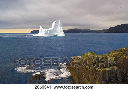Stock Image - Iceberg Floats In Trinity Bay Off The Bonavista Peninsula With Rocky Shoreline, Eastern Newfoundland. Fotosearch