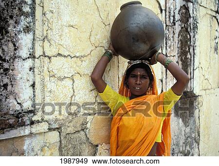 Stock Photo - India, Jaipur, Indian Woman Leans Agianst Wall, Ceramic Pot Atop Head No Model Release. Fotosearch