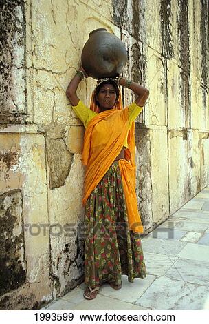Stock Photo - India, Jaipur, Indian Woman Leans Agianst Wall, Ceramic Pot Atop Head No Model Release. Fotosearch