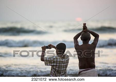 India, Karnataka, Hindu Pilgrim Praying By Ocean While Boy Is Photographing; Gokarna View Large Photo Image Stock Image - India, Karnataka, Hindu Pilgrim Praying By Ocean While Boy Is Photographing; Gokarna. Fotosearch