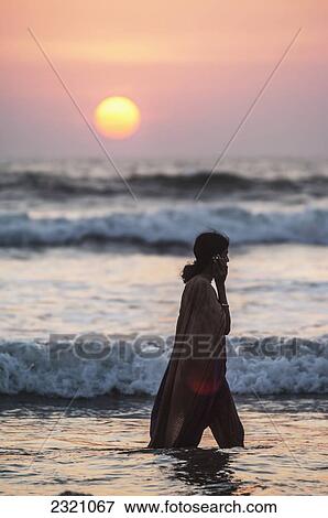 Stock Photo - India, Karnataka, Indian Girl Walking In Sea Talking On Mobile Phone At Sunset; Gokarna. Fotosearch