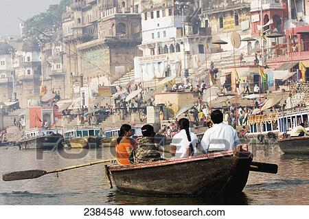 Stock Photo - Indian family being rowed along the holy, but polluted, River Ganges, passing bathing ghats; Uttar Pradesh, India. Fotosearch