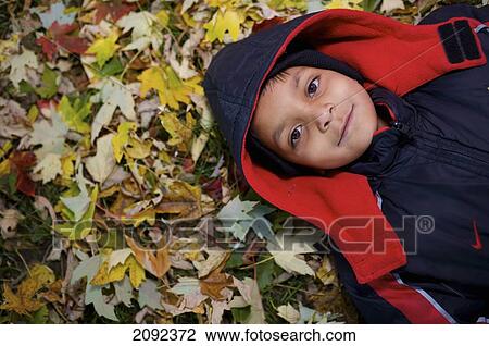 Stock Image - Indian Girl Lying In Autumn Leaves Outside Esl School; Guelph Ontario Canada. Fotosearch