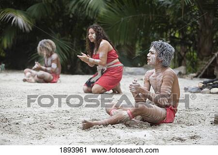Stock Image - Indigenous People Siting On The Sand Clapping And Singing; Queensland, Australia. Fotosearch