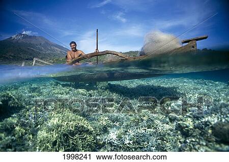 Stock Image - Indonesia, Bali, Fisherman In Wooden Boat, Fishing Net, Volcano Background Over/Under. Fotosearch