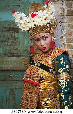 Stock Photo - Indonesia, Bali, Legong dancer next to a traditional Balanese gate in Ubud. Gates such as these are thought to be a barrier to evil spirits entering home; Ubud. Fotosearch