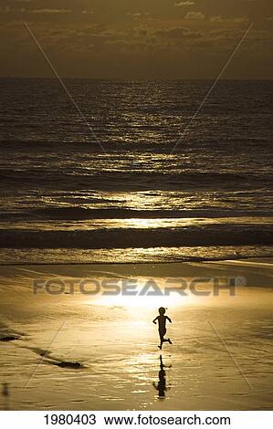Stock Image - Indonesia, Bali, Silhouette of boy running on beach; Semniyak. Fotosearch