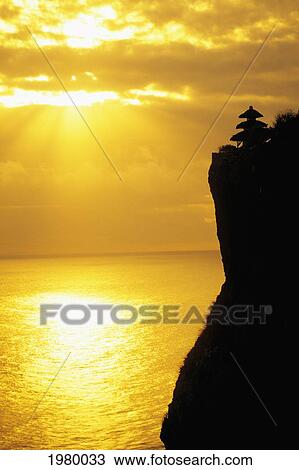 Indonesia, Bali, Uluwatu Temple Silhouetted In Distance Along Cliff, Golden Sunset Reflections On Ocean. View Large Photo Image Stock Image - Indonesia, Bali, Uluwatu Temple Silhouetted In Distance Along Cliff, Golden Sunset Reflections On Ocean.. Fotosearch