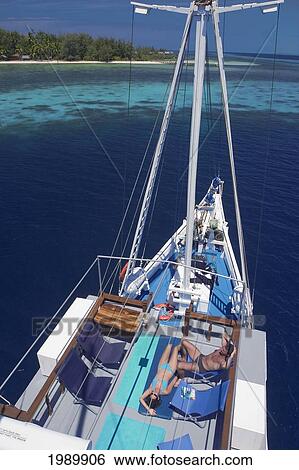 Stock Photograph - Indonesia, Raja Ampat Islands, Couple Sunbathes On Deck Of Live-Aboard Dive Boat.. Fotosearch