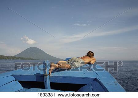 Stock Image - Indonesia, Sulawesi, Man Sunbathing on Boat; Manado Tua. Fotosearch