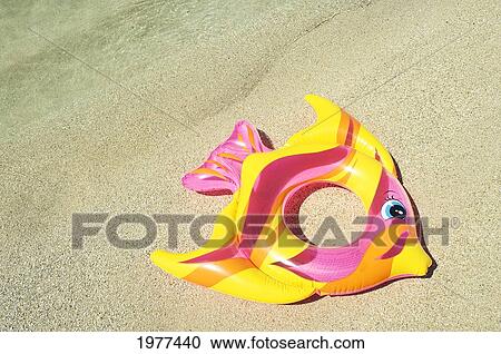 Stock Image - Inflatable Fish Ring In Pink, Yellow And Orange, Laying On Sand.. Fotosearch