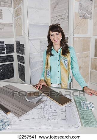 Stock Image - Interior designer selecting tiles in showroom of tile store and texting on phone; Edmonton, Alberta, Canada. Fotosearch