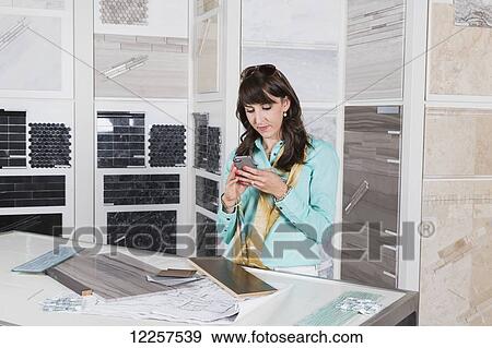 Stock Photo - Interior designer selecting tiles in showroom of tile store and texting on phone; Edmonton, Alberta, Canada. Fotosearch