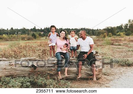 Stock Image - Interracial Family Sitting On Log On Beach; British Columbia, Canada. Fotosearch