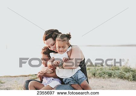 Stock Photo - Interracial Mother And Daughters Relaxing On The Beach; British Columbia, Canada. Fotosearch