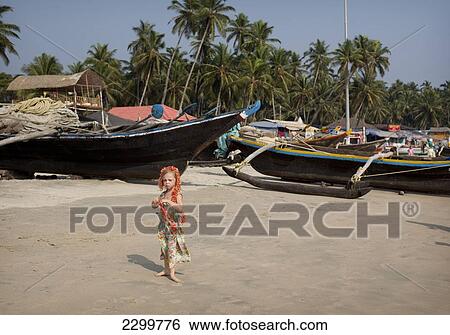 Stock Photograph - Isla Reynolds 4 years old stands in front of the many traditional boats and beach front restaurants that line Palolem beach, Goa, India.. Fotosearch