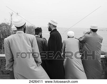 Stock Image - Islamic men stand at a railing looking out over the Bosphorus; Istanbul, Turkey. Fotosearch