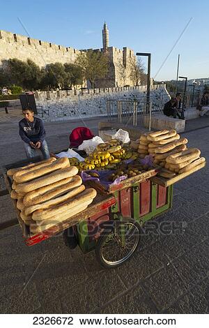 Stock Image - Israel, Jerusalem Old City, Youngster hawker selling bagel bread at stall with Citadel of David in background; Jerusalem. Fotosearch