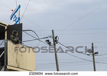 Picture - Israeli soldier on mirador with projectors in background; Israel. Fotosearch