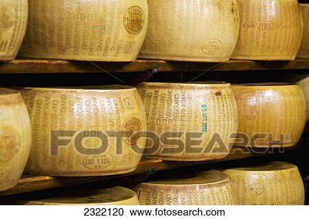 Stock Image - Italy, Emilia-Romagna, Bologna, Close up of Reggiano Parmigiano cheese wheels on shelves. Fotosearch