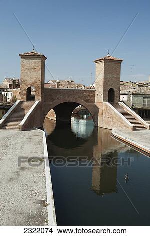 Picture - Italy, Emilia-Romagna, Comacchio, Stone bridge with towers and steps reflecting in water. Fotosearch