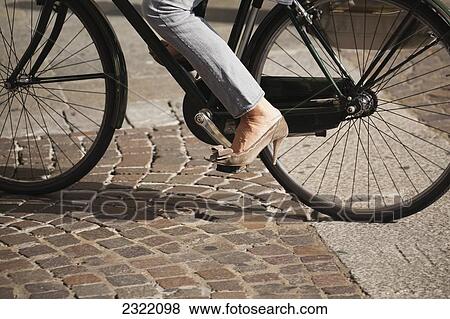 Stock Photo - Italy, Emilia-Romagna, Parma, Low section of female cyclist wearing high heeled shoes cycling on cobblestone. Fotosearch