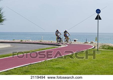Picture - Italy, Marche, Men cycling on bicycle lane with view of sea; Lido Tre Archi. Fotosearch