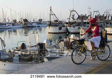 Italy, Marche, Woman on bicycle looking at sunset in fishing port; Porto San Giorgio View Large Photo Image Stock Image - Italy, Marche, Woman on bicycle looking at sunset in fishing port; Porto San Giorgio. Fotosearch