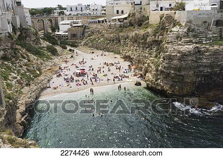 Stock Photograph - Italy, Puglia, Polignano a Mare beach is a picturesque swath of golden sand that slips into bright clear green water and is lined by sheer cliffs. There are many sea caves and small coves; Polignare del Mare. Fotosearch