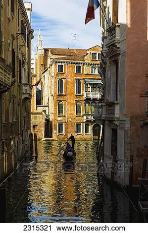 Stock Image - Italy, Venice, Rowing gondola through canal. Fotosearch