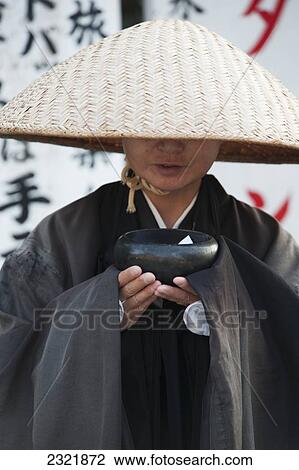 Stock Image - Japan, Kyoto, Woman wearing conical hat and black robe and holding bowl. Fotosearch