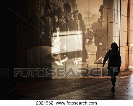 Stock Image - Japan, Tokyo, Woman walking by large picture displayed on wall along walkway. Fotosearch