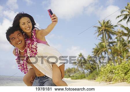 Japanese Couple On The Beach Wearing Leis Takes Photo Of Themselves With Camera Phone. View Large Photo Image Stock Image - Japanese Couple On The Beach Wearing Leis Takes Photo Of Themselves With Camera Phone.. Fotosearch