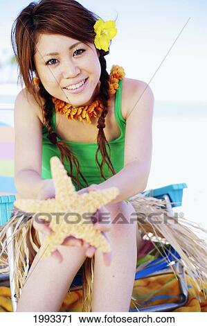 Stock Image - Japanese Girl In Hula Skirt Holding Out A Starfish. Fotosearch