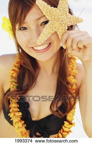 Picture - Japanese Girl With Lei Holding Starfish Up To Her Eye. Fotosearch