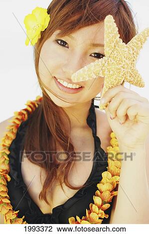 Stock Image - Japanese Girl With Lei Holding Starfish Up To Her Eye. Fotosearch
